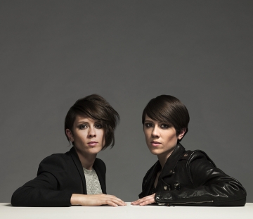 Medium shot of Tegan and Sara sitting at a table with a grey background.