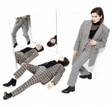Tegan and Sara in black and white patterned suits, on a white background with mirrored reflections.