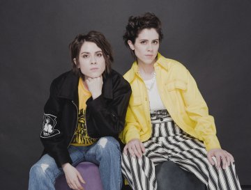 Tegan and Sara, Tegan wearing a black jacket and yellow t-shirt, Sara wearing a yellow jacket with a white t-shirt.